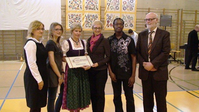 Ehrengäste und Schüler/innen freuen sich, als Dir. Cornelia Polli das Zertifikat von Fr. LR Hummer verliehen bekommt.