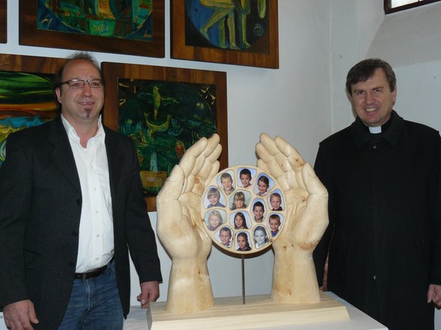 Künstler Hans-Peter Rainer und Pfarrer Mag. Georg Gerstmayr mit den kunstvoll geschnitzten Händen, die schützend die Bilder der Erpfendorfer Erstkommunikanten halten