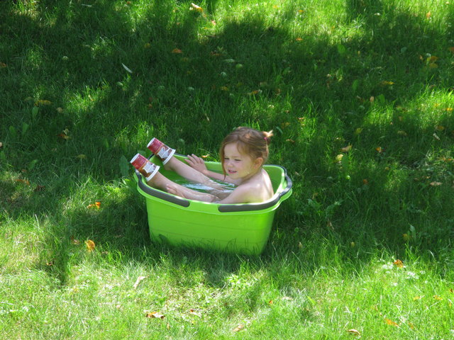 Anna in der grünen Wanne mit 2 Joghurtbecher auf den Füßen zum Spielen.