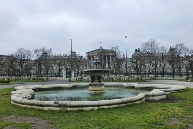 Derselbe Brunnen nochmals, diesmal mit dem Gitterzaun und dem Parlament als Hintergrund