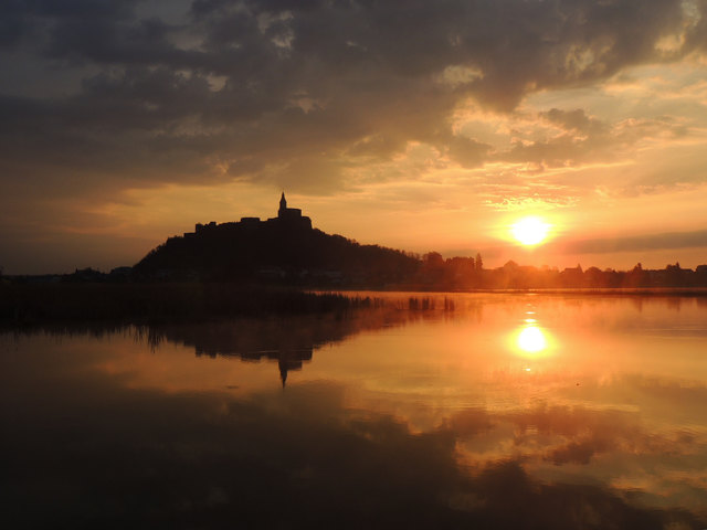 Während sich die historische Burg im ruhigen Wasser der Güssinger Fischteiche spiegelt, begrüßt die aufgehende Sonne den neuen Tag.