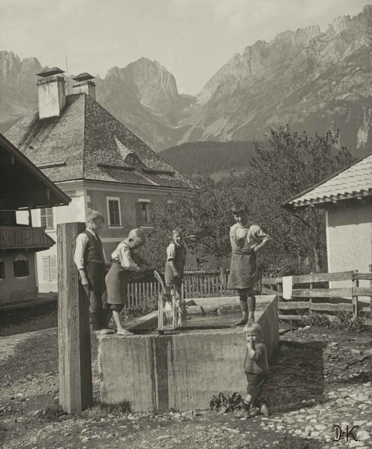 Kinder am Dorfbrunnen in Going vor dem Kaisergebirge mit Ellmauer Tor.