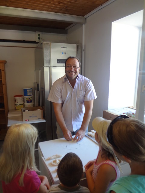 Bäckermeister Berger im Kreise interessierter Kinder bei der Vorbereitung von Teiglingen