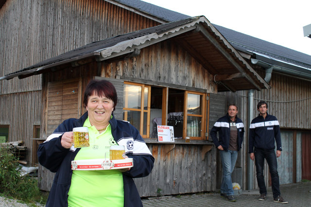 Frieda Rannetbauer vor der nach ihr benannten Hütte: „Der Zickl-Mami-Hüttn“. Von dort aus versorgt sie bei Heimspielen die Zuschauer mit Getränken. Im Bild hinten, Kampfmannschafts-Trainer Gerhard Ecker und Kapitän Johannes Kehrer, der nicht mit ihr verwandt ist, sie aber „Tante Frieda“ nennt.