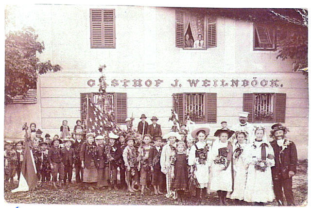 Dieses Bild von 1905 zeigt eine Kinderschar in festlicher Bekleidung vor dem ehemaligen Schloss Velden, Marktplatz 1 in Neufelden. Nach der Hopfenernte, dem "Hopfnbedln", wurde jährlich ein Hopfenfest gefeiert. Das Hofenkönigs-Paar steht in der Reihe ganz rechts. Der Herr dahinter ist Josef Weilnböck, der damalige Besitzer des Gasthofes sowie des Hopfenlagers/der Hopfendarre.