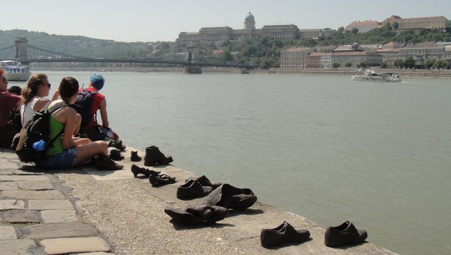 Die Bronze-Schuhe sind ein ungewöhnliches Holokaust-Denkmal. Die ungarischen Nazis, Mörder, Pfeilkreuzler, haben im Winter 1944/45 jüdische MitbürgerInnen an die Donau getrieben und mit einem Genickschuss in die eisigen Fluten befördert. Vorher mussten sich die Opfer alles Brauchbare ausziehen und zusammenlegen. Heute pilgern vor allem junge Leute und viele ausländische BesucherInnen zu diesem erschütternden Mahnmal.