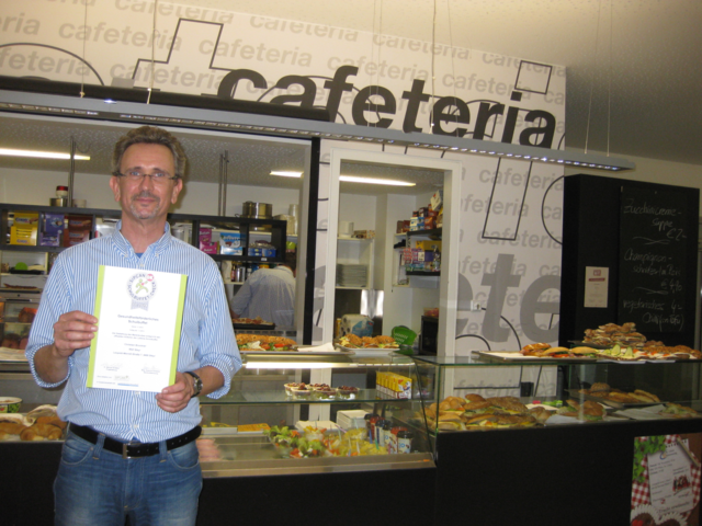 Christian Bruckner mit der verliehenen Auszeichnung vor dem modern gestalteten Buffet der HLW und HAK Steyr