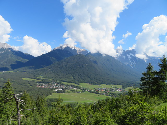 Blick auf Nisskogel (Bildmitte), Grünstein (links dahinter) und Wankspitze (die rechts ihren Gipfel in Wolken hüllt). Davor, inmitten von Wald und Wiesen Ortsteile von Obsteig