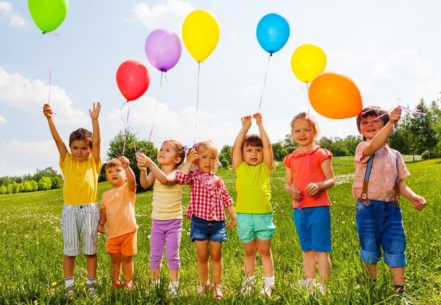 Seven children with balloons in green field