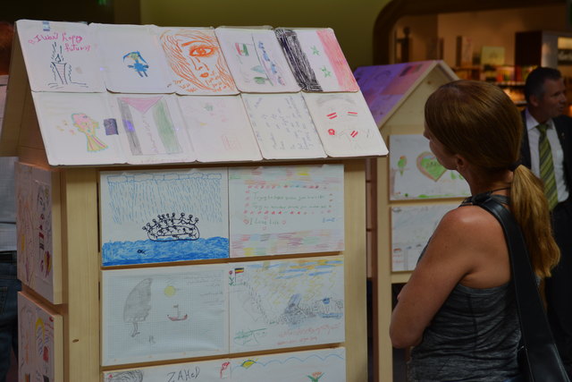 Auf insgesamt fünf Holzhäuschen zeigt das Rote Kreuz Bilder von Menschen auf der Flucht.