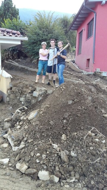 Daren Quinton und Ethan Kitsel mit Birgit Kahlhofer vor einem Haufen den sie von einem für Bagger unzugänglichen Hausbereich nach vorne geschafft haben.