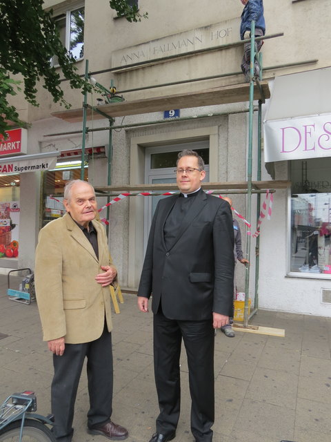 Walter Bergolth und Pfarrer Alipius Müller vor dem jetzt renovierten Gebäudeschild von Anna Fallmann.