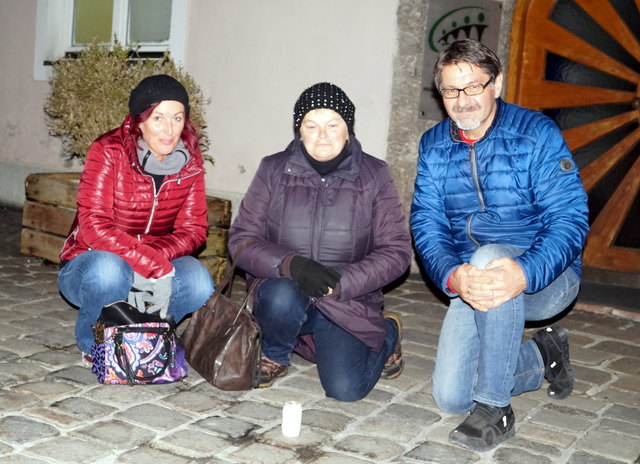 Gabriele Klee, Halina Höller und Walter Reschreiter zünden eine Kerze an einem Stolperstein in der Pfarrgasse an.