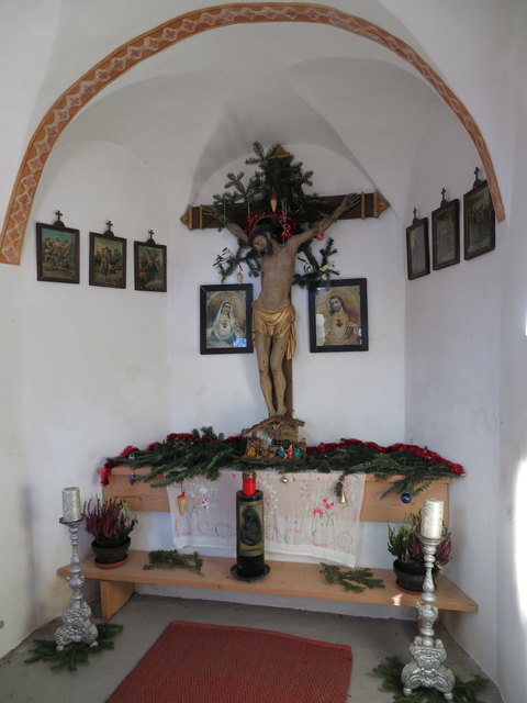 Im Inneren der liebevoll geschmückten Kapelle kann man durch ein kleines Fenster das schöne Kruzifix aus der ersten Hälfte des 19.Jahrhunderts bewundern