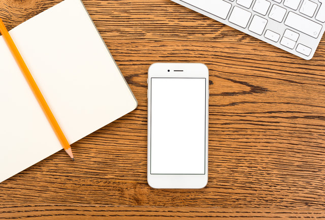Modern smartphone with blank display on the desk of workplace. Top view.