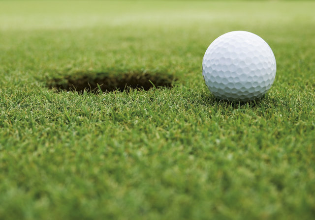 Golfball liegt neben Loch auf Rasen