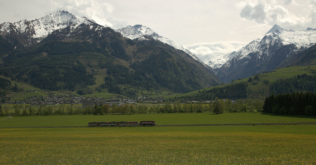Kaprun mit den verschneiten (v.L.) Imbachhorn den Bratschenkopf und dem Kitzsteinhorn. Im Vordergrund die Pinzgau Lokalbahn.