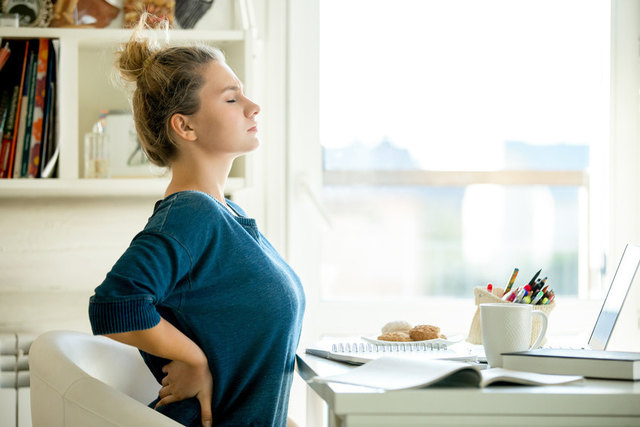 Portrait of an attractive woman in a chair at the table with cup and laptop, book, pencils, notebook on it. Concept photo