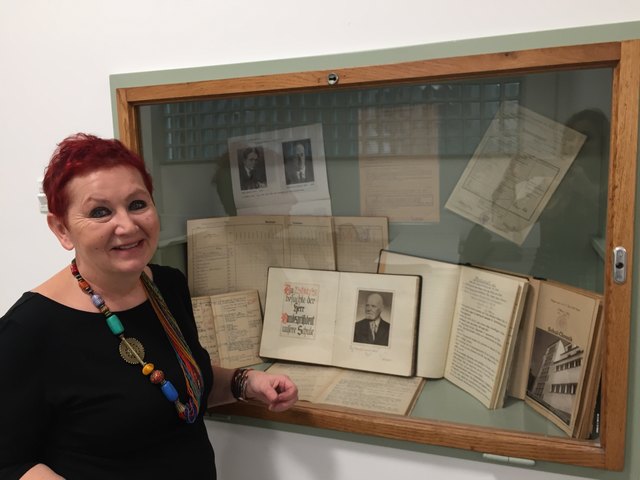 Direktorin Andrea Hallal-Wögerer vor einem Schaukasten, der Fotos und Berichte aus den Anfangstagen der Schule enthält.