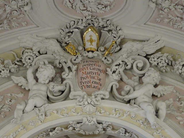 Der Innsbrucker Baumeister Georg Anton Gumpp hat das Alte Landhaus, das heute als einer der prächtigsten barocken Bauten Innsbrucks gilt, und damit auch die Kapelle in den Jahren 1725 bis 1728 errichtet. Diese von Putten gerahmte Kartusche mit lateinischem Text zeigt die Jahreszahl 1731