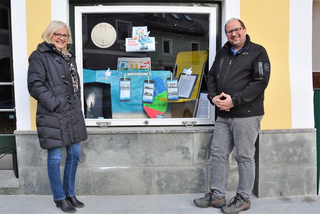 Lehrerin und Projektleiterin Gudrun Kern und NMS-Direktor Richard Schulz-Kolland vor dem von Schülerinnen und Schülern gestalteten Schaufenster des ehemaligen Cafés Rubinigg am Dorfplatz St. Michael.