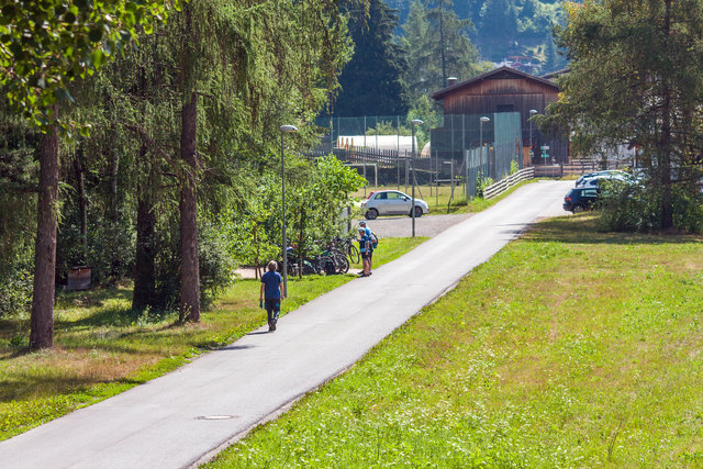 Der Innradweg (Route Nr. 1) und Radweg Via Claudia Augusta (3. Etappe - Nr. 32) zwischen Landeck und Nesselgarten (Fließ) setz sich hier noch am orographisch linken Ufer fort und vorbei am Franziskus- Rastplatz (dort wo man Radfaherer stehen sieht). Im Hintergrund nach dem kleinen Fußballfeld sieht man die Rampe zur Holzbrücke über den Inn. Dort wird die Seite für einen ca. 3 km langen Abschnitt gewechselt, weil auf der orographisch linken Seite der Radweg nicht fortgesetzt werden kann. | Foto: © by Ing. Günter Kramarcsik