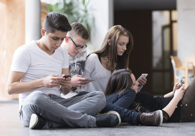 Vier Jugendliche sitzen auf dem Boden und schauen in ihr Smartphone. | Foto: MEV