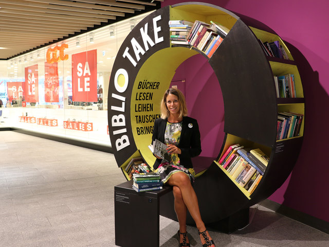 Center-Managerin Verena Wegscheider sitzt auf der Bank des "Biblio-Take", wo man Bücher kostenlos mitnehmen und gelesene Bücher hinbringen kann. | Foto: Forum 1