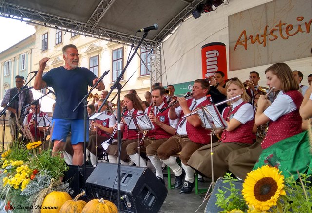 Für Arnold Schwarzenegger ging es nach dem Besuch im Fitnessstudio per E-Bike kurz zum Aufsteirern auf den Karmeliterplatz. Dort überraschte er mit seinem Erscheinen auf der Bühne die Marktmusikkapelle Bad Waltersdorf. „Die steirische Eiche“ dirigierte spontan einen ganzen Marsch und erntete dafür viel Beifall vom erstaunten Publikum. Der legendäre Terminator erzählte stolz von seinem Vater als Musiker in einer Blaskapelle und radelte dann zusammen mit seinen Begleitern eilig davon.