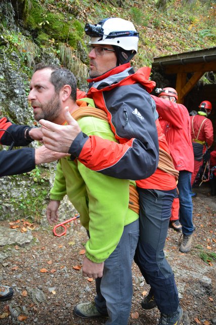 Eine Person trägt einen Verletzten mit dem Seil aus der Höhle.