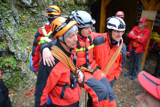 Zwei Personen tragen eine Verletzte mit dem Seil aus der Höhle.