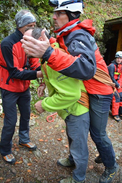 Eine Person trägt einen Verletzten mit dem Seil aus der Höhle.