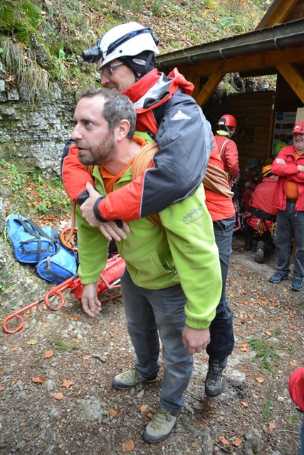 Eine Person trägt einen Verletzten mit dem Seil aus der Höhle.