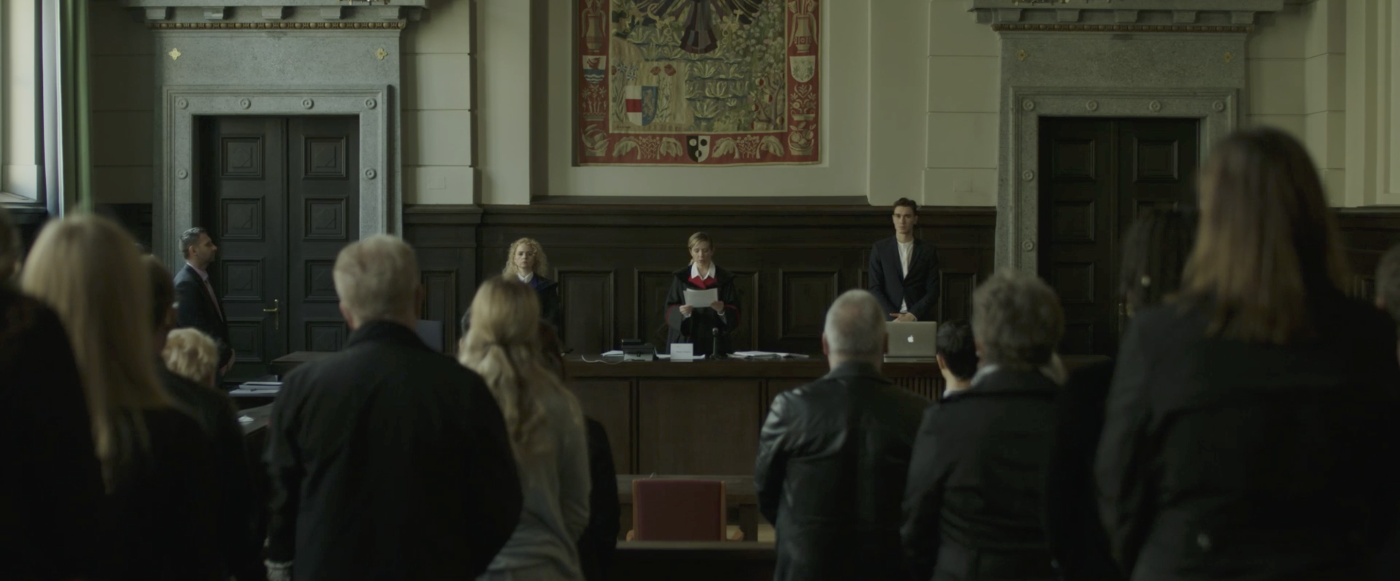 "Das Urteil im Fall K.". Es zeigt eine Szene aus dem Gerichtssaal in St. Pölten. Martina Poel spielt die Richterin.