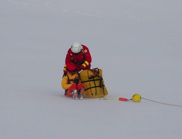 Schützend vor dem Schneewirbel des landenden Hubschraubers wird dem Verletzten die Kapuze des Anoraks übers Gesicht gezogen und die Hand beruhigend auf die Schulter gelegt.