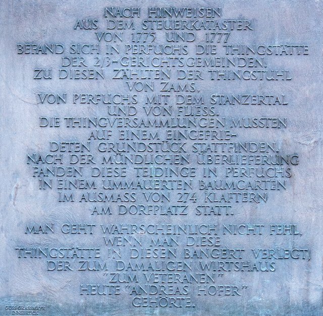 Bild 52: An der SO- Ecke der historischen Einfriedungsmauer befindet sich diese Informationstafel.
Hier ist zu lesen:
Nach Hinweisen aus dem Steuerkataster von 1775 und 1777 befand sich in Perfuchs die Thingstätte der 2/3- Gerichtsgemeinden. Zu diesen zählten der Thingstuhl von Zams, von Perfuchs mit dem Stanzertal und von Fließ.

Die Thingversammlungen mussten auf einem eingefriedeten Grundstück stattfinden. Nach der mündlichen Überlieferung fanden diese Teidinge in Perfuchs in einem ummauerten Baumgarten im Ausmaß von 274 Klaftern (1 Klafter = 3,5979 m² = 985,82 m²) am Dorplatz statt.

Man geht wahrscheinlich nicht fehl, wenn man diese Thingstätte in diesen Bangert (Anm.: Mundart für Baumgarten) verlegt. Der zum damaligen Wirtshaus "zum Veteranen" und heute (Anm.: gilt nicht mehr, weil nun ein Wohnhaus) "Andreas Hofer" gehörte.  | Foto: © by Ing. Günter Kramarcsik