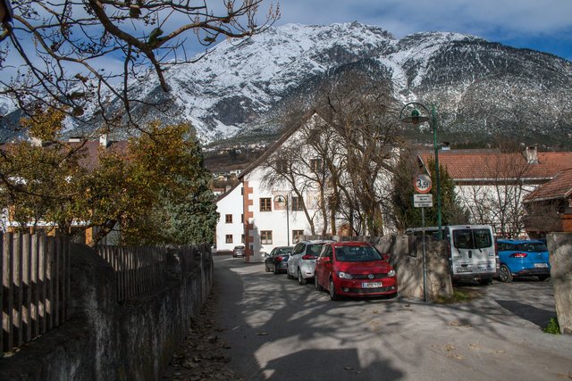 Bild 55: Durchsicht vom Dorfplatz nach Norden. Links hinter den Thyen ist Haus Nr. 37. Gegenüber ist Haus Nr. 36  (ehemaliger Gasthof Andreas Hofer). Dahinter ist Haus Nr. 38 (Gablhaus). 
Rechts im Vordergrund ist die Thingstätte, welche heute als Parkplatz genutzt wird und für diesen Zweck die historische Einfriedung als Zufahrtsöffnung teilweise abgebrochen wurde. | Foto: © by Ing. Günter Kramarcsik
