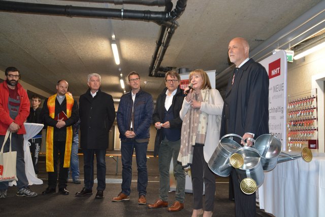Festakt zur Schlüsselübergabe (v. li.) mit Dekan Peter Scheiring, GV HR Josef Federspiel, Bgm. Christian Härting, NHT-Geschäftsführer Hannes Gschwentner, LR Dr. Beate Palfrader und Künstler Franz Wassermann mit drei Gießkannen, die verteilte er an Bgm. Härting, NHT-GF Gschwentner und den Hausmeister als Vertreter der Bewohner, sie sollen damit den umgekerht eingepflanzten Baum "Die Vertriebenen" zum Erblühen bringen.