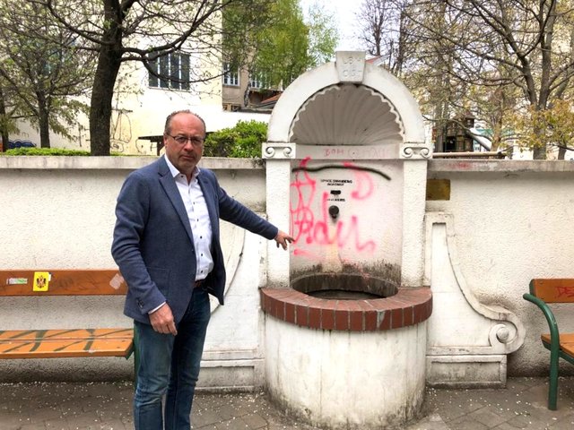 Der ÖVP-Bezirksrat Karl Gödde weist auf die Verunstaltung des Brunnen. Der Eingangsbereich soll neu gestaltet werden.