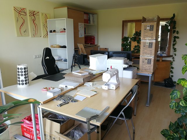 Das 18 m² Büro dient als Lager, Fotostudio, Buchhaltung, Ablage, Kreativwerkstatt und alles, was es sonst noch sein muss. Eines der zentralen Elemente ist die Verpackung, die die beiden Schreibtische im Vordergrund einnehmen. Auch die Nähmaschine ist zu sehen.