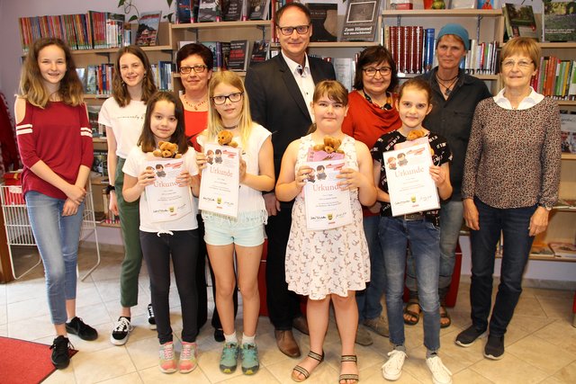 Gruppenfoto mit Siegerinnen, Juroren, Büchereiteam und Vorstandsmitglied Werner Zuschnegg. Ivana Tatzer, Jasmin Ploder, Julia Kögler und Stella Wille (vorne von rechts) haben den kleinen Bären mit roter Masche sehr glücklich gemacht.