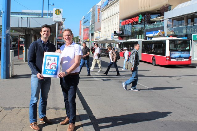 Bernhard Herzog (l.) und Josef Fischer (beide SPÖ) mit einem Begegnungszone-Schild am Franz-Jonas-Platz. Hinter ihnen ist der Bereich der zur Begegnungszone werden soll.