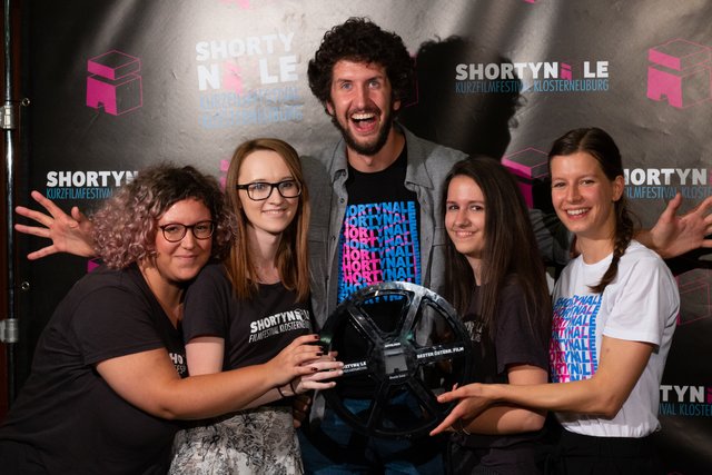 Der	Filmschaffende	Alexander	Gratzer	(Mitte)	hat	gleich	zwei	Mal	mit	seinem	Film	“Apfelmus”	abgeräumt.	
Mit	seinen	beiden	Urkunden	posiert	er	mit	dem	Festivalteam:	Aleksandra	Antic,	Marion	Schlosser,	Anna	
Wagnleitner	und	Flora	Mair	 | Foto: 	Shortynale	Team	(Theresa	König,	Limara	Wriesnig	&amp;	Markus	Löbl)