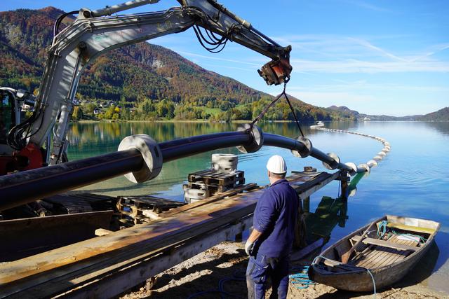 Die neue Abwasserleitung wird mit einem Bagger hochgehoben und in den Fuschlsee hineingeschoben.