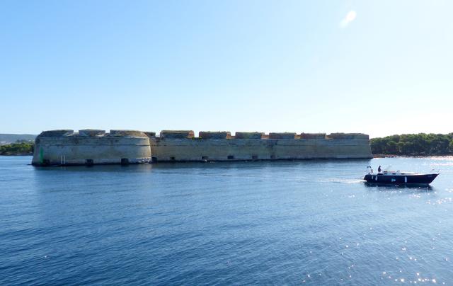 Schützendes Bollwerk mitten im Meer – die Nikolausfestung vor Sibenik: diese wehrhafte Festungsanlage wurde zur Abwehr der Türken errichtet. Der venezianische Architekt der Spätrenaissance Michele Sanmicheli war der Baumeister dieses Kastells. Bemerkenswert sind die im Mauerwerk ausgesparten Öffnungen für Kanonen, denn sie liegen in etwa auf dem gleichen Niveau wie das Meer. Somit konnten die auf Schiffen herannahenden Feinde an ihren empfindlichsten Stellen getroffen werden – direkt über der Wasserlinie, was nach einem gut gezielten Schuss ein rasches und erbarmungsloses Sinken zur Folge hatte. Die Nikolausfestung wird von allen Seiten vom schützenden Meer umgeben. Nur ein schmaler Damm verbindet das Gemäuer mit dem Festland, was es so gut wie uneinnehmbar machte. Nicht von ungefähr zählt die Festung St. Nikola zu den mächtigsten und stärksten maritimen Befestigungsanlagen an der Adriaküste.
Am eindrucksvollsten wirkt die Festung, wenn Sie sich ihr vom Meer aus nähern. Die dicken hohen Mauern vermitteln den Eindruck, als seien sie mit dem Meeresboden verwachsen.