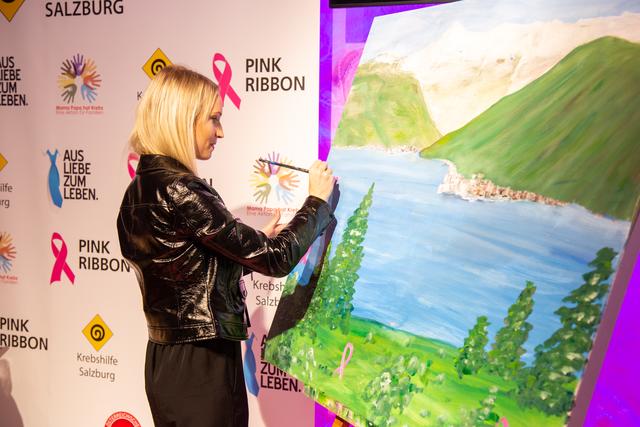 Julia Buchner malt eine pinke Schleife auf das Bild von Sabine Schreckeneder. | Foto: Nikolaus Faistauer Photography