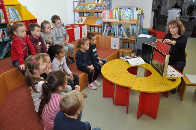Kinder des städtischen Kindergartens Taschelried erleben eine Kamishibai-Erzählung in der Stadtbücherei. Dabei wird eine Geschichte vorgelesen, die Bilder dazu werden in einer aufklappbaren Holzbühne präsentiert.