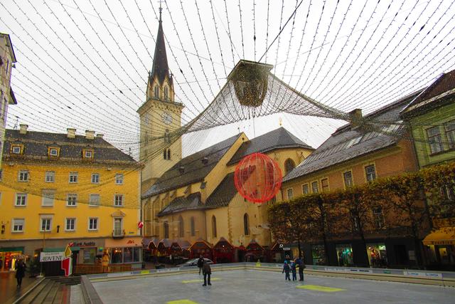 nur wenige Eisläufer tummeln sich bei Regen am Eisplatz vor dem Rathaus, der Advent- und Weihnachtsmarkt in Villach um die Stadtpfarrkirche ist eröffnet. 