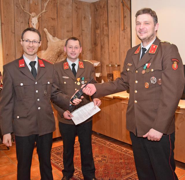 Der langjährige Lotsenkommandant Bernhard Seidl (rechts) übergab diese Funktion an Manuel Reischl (links) symbolisch mit einem Einsatzfunkgerät. Bildmitte: Kommandant HBI Christian Ameseder