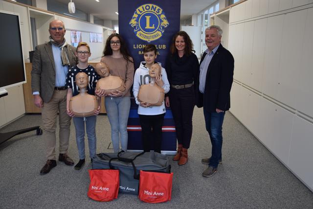Lions-Präsident Christof Kravutske, Daniel Zuk, Kiara Lamisch, Jamie-Noah Torskyj, Lehrerin Petra Kolm BEd und NMS-Direktor Wolfgang Loidl-Kendler bei der Übergabe der Übungspuppen.